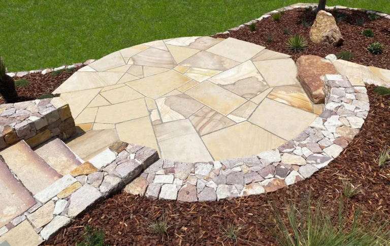 Stone patio with plants and green lawn.