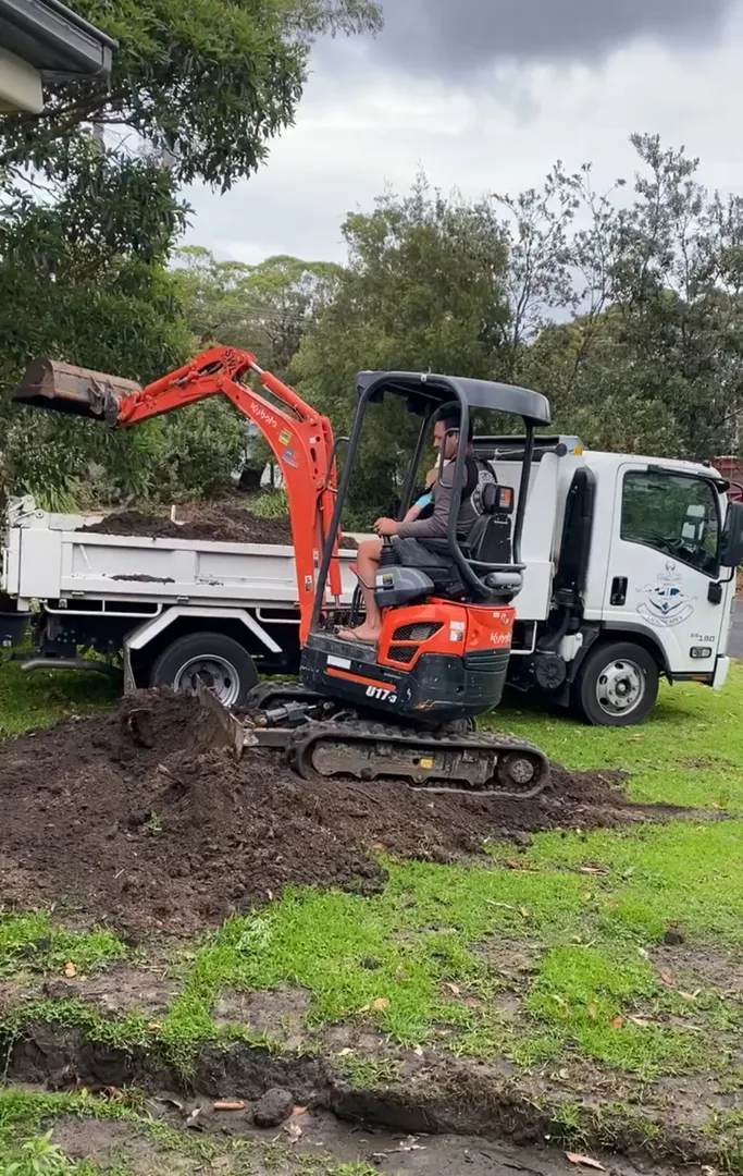 Mini excavator moving soil in a garden area.