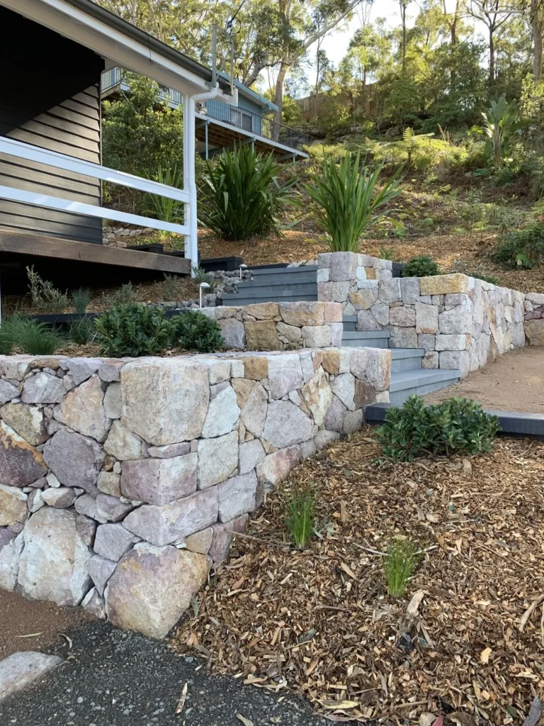 Stone retaining wall with plants and house