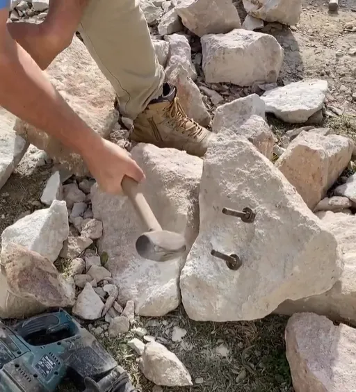 Man hammering stone wedges for splitting rock