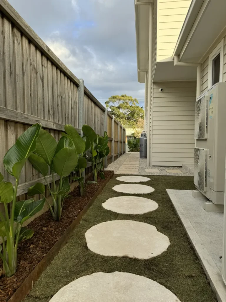 Pathway with round stones beside house and plants.