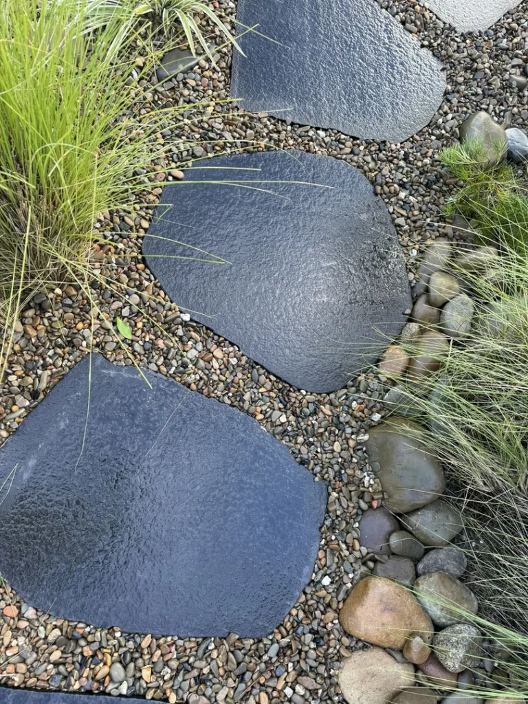 Black stepping stones on pebble and grass path.