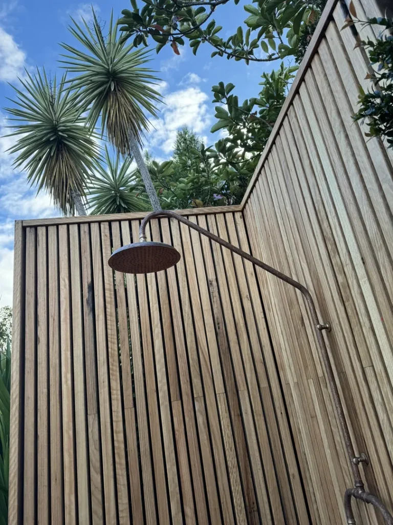 Outdoor shower with wooden enclosure and palm trees.