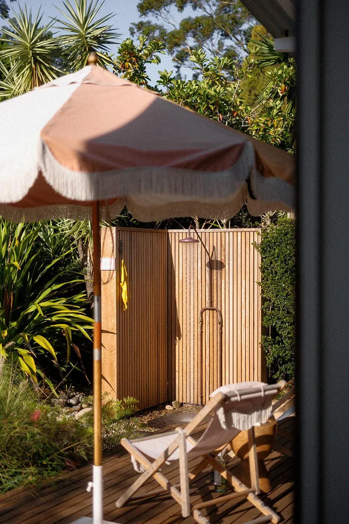 Outdoor shower with umbrella and chair nearby.