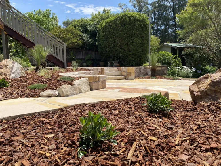 Sunny backyard with mulched garden and stone pathway.