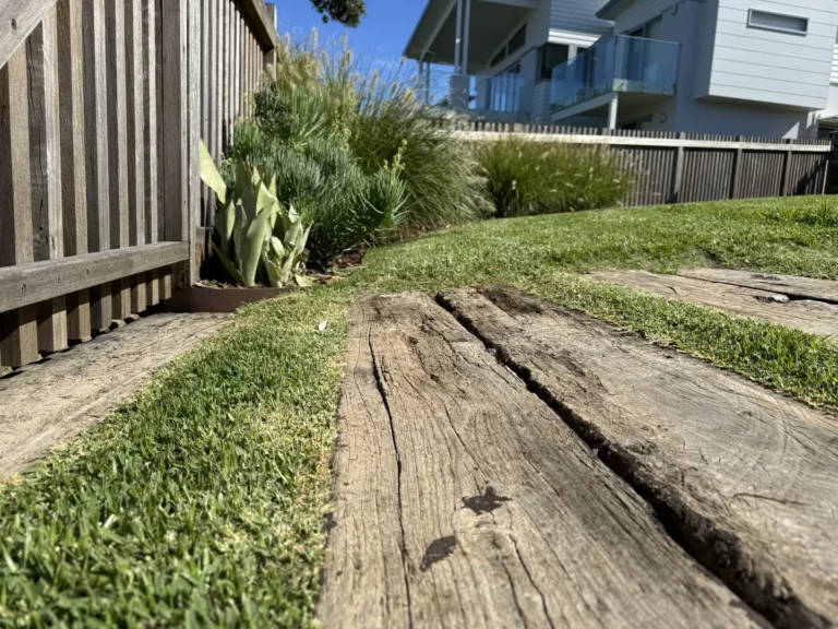 Wooden garden path beside modern home and lawn